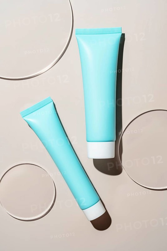 Blue cosmetic tubes artfully placed on a smooth surface, featuring soft shadows and circular surface. The minimalist design emphasizes modern elegance and clean lines