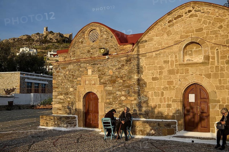 Elderly people chatting in front of a historic building as the afternoon sun casts shadows, Easter 2025, Church of the Dormition of the All-Holy God Bear, Kimisis tis Theotokou, Asklipio, Rhodes, Dodecanese, Greek Islands, Greece