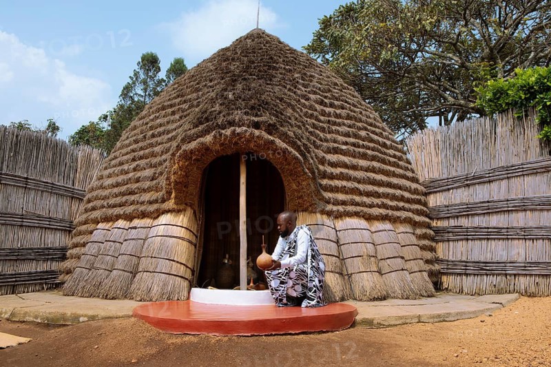 Rwandan man, 25 years old, wearing traditional clothing at the entrance to the beehive shaped beer house, Royal Palace, Nyanza, Rwanda