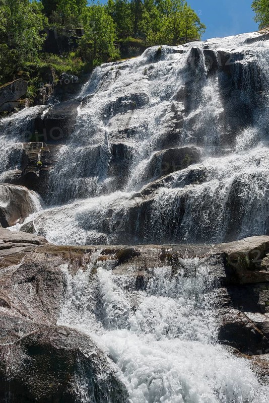 A majestic waterfall flows in several cascades over rocks, surrounded by trees in sunny weather, Cascada del Caozo, Garganta de Bonal de los Llanos, Piornal, Cáceres, Cacares, Extremadura, Spain