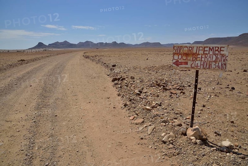 Hand-painted advertising sign for a liquor store on a dirt road in a barren landscape, Orupembe, Kaokoland, Kunene, Namibia
