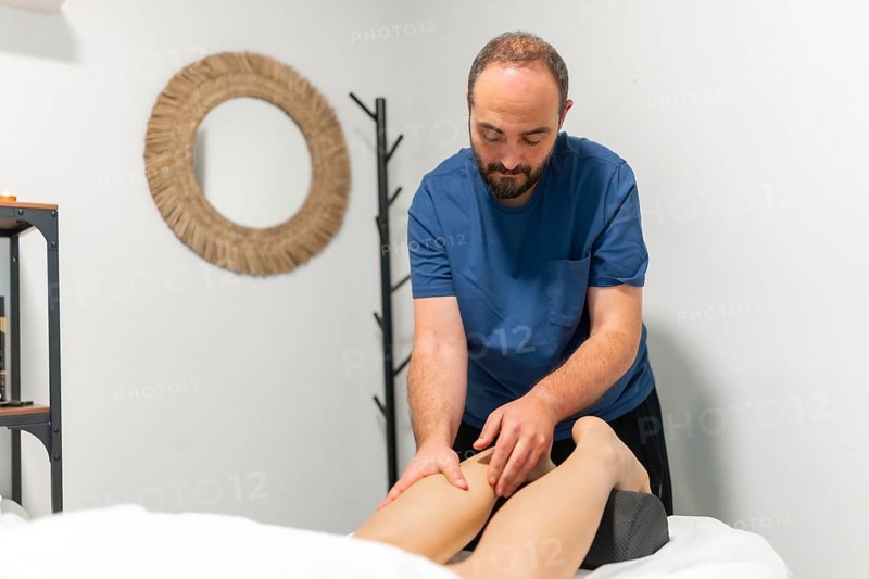 Masseur giving a professional leg massage to a client, providing relaxation and muscle recovery during a rehabilitation session in a clean spa or therapy room setting