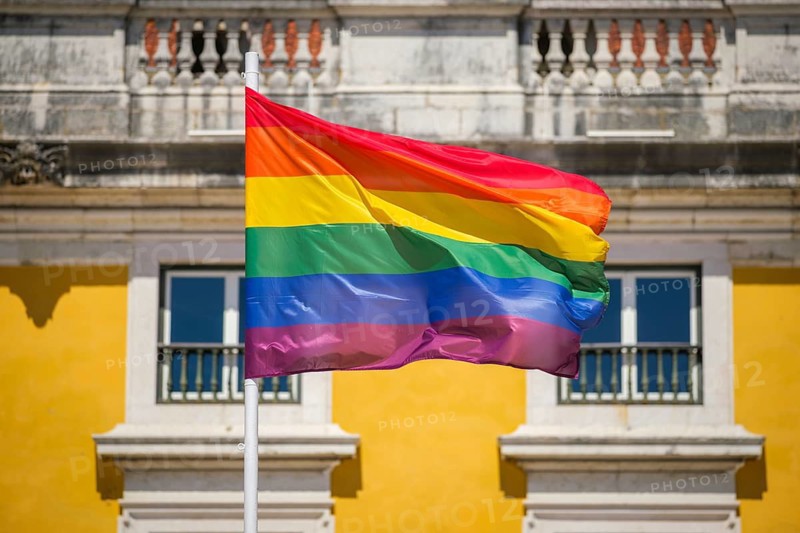 Rainbow pride colors wave on a traditional pride flag in the Lisbon, Portugal sky for LGBT equality, photographed against wispy clouds