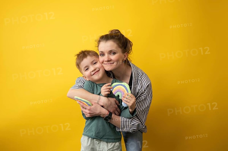A joyful teacher hugs her smiling student as they proudly display rainbow crafts. The warm, affectionate moment is captured against a bright yellow background, symbolizing creativity and care