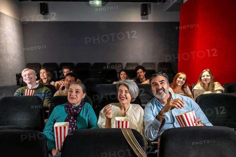 People of different ages and ethnicities are watching a film and eating popcorn in a movie theater, experiencing a shared moment of entertainment