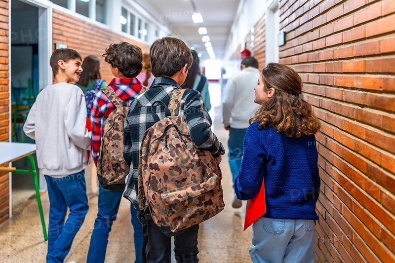 Group of elementary school students walking in the hallway between classes, chatting and carrying backpacks