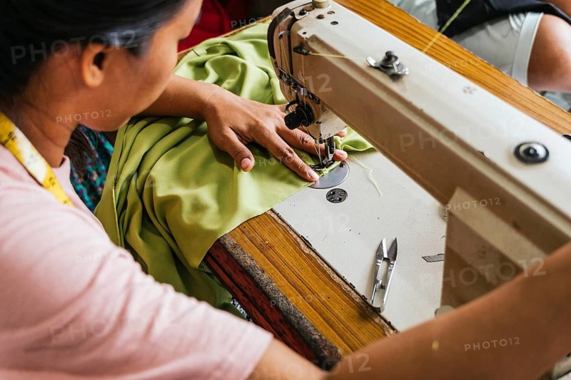 A asian seamstress skillfully sewing green fabric using a sewing machine. The workspace is equipped with essential tools like scissors and a measuring tape, highlighting craftsmanship