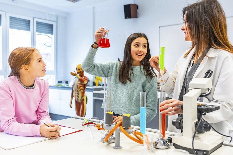 Female teacher showing chemical reaction to students during experiment in school chemistry laboratory