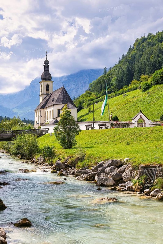 Parish church of St Sebastian by a river in an idyllic Alpine landscape with mountains and forests in the background, Ramsau, Berchtesgadener Land, Upper Bavaria, Bavaria, Germany