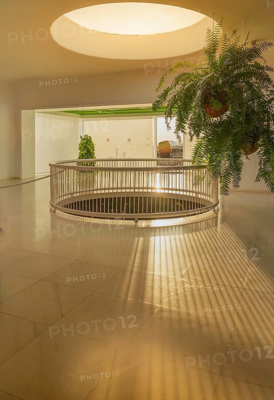 Serene indoor space with modern architecture featuring sunlit floors, a circular railing, and lush greenery in a typical building in Lanzarote, Canary Islands, Spain, ideal for tourism