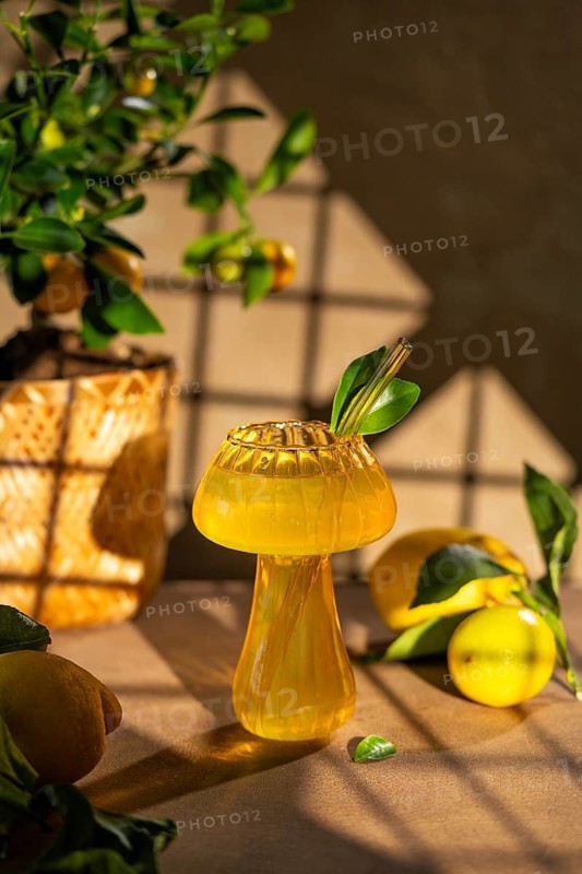 A bright and refreshing lemon drink served in an elegantly designed glass, complemented by fresh lemons and green leaves, sitting in warm, natural sunlight