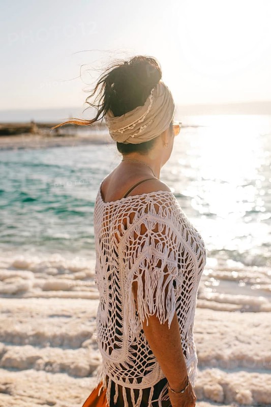 Side view of unrecognizable woman with a headscarf gazing towards the sunlit horizon over Dead Sea in Jordan, symbolizing serenity and wanderlust
