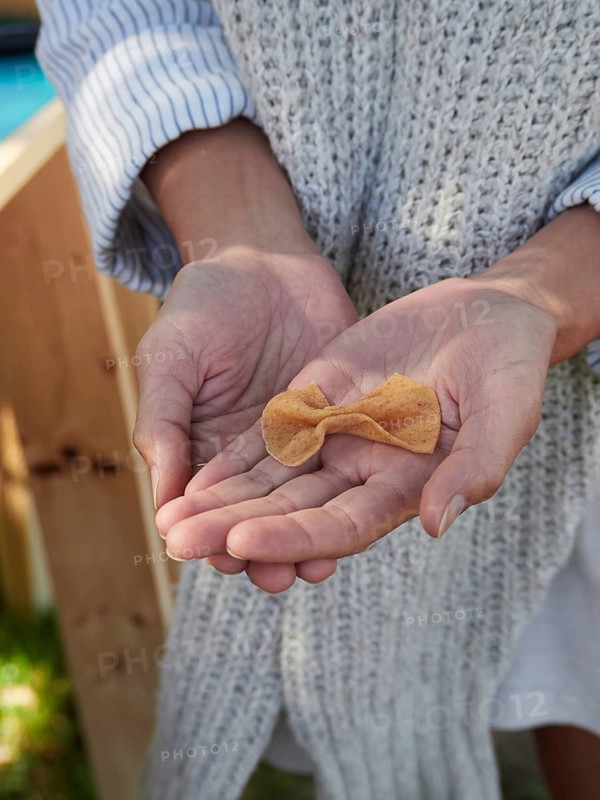 Top view of anonymous female in sweater while standing in shadow showing bow tie shaped farfalle pasta dish in palm against blurred wooden table and green grass ground in daylight
