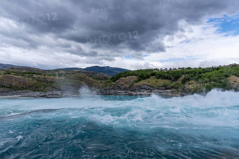 Confluence of Río Baker and Río Neff, turquoise blue water with rapids and spray, cloudy sky over wooded hills, Aysén region, Patagonia, Chile