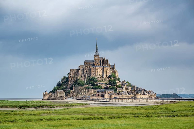 View over lush green salt marshes to the rocky island, Le Mont Saint Michel monastery island with the former Benedictine abbey in Norman style, tourist attraction, UNESCO World Heritage Site, Pontorson, Manche department, Normandy, France