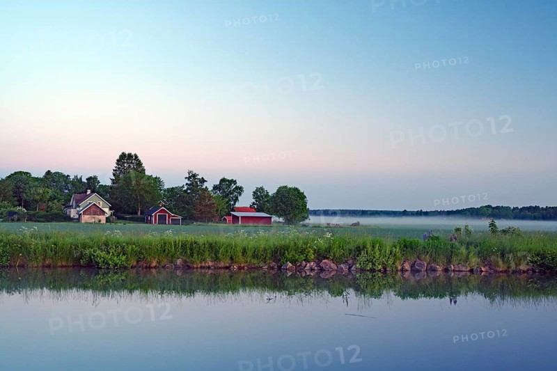 Morning light over a quiet lake with houses and fog in the surrounding countryside, Göta Canal, Töraboda, Västra Götalands län, Sweden
