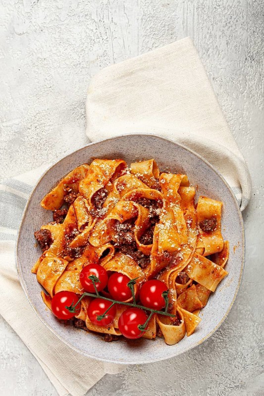 Pappardelle pasta with bolognese sauce, topped with parmesan cheese and cherry branch, homemade, no people