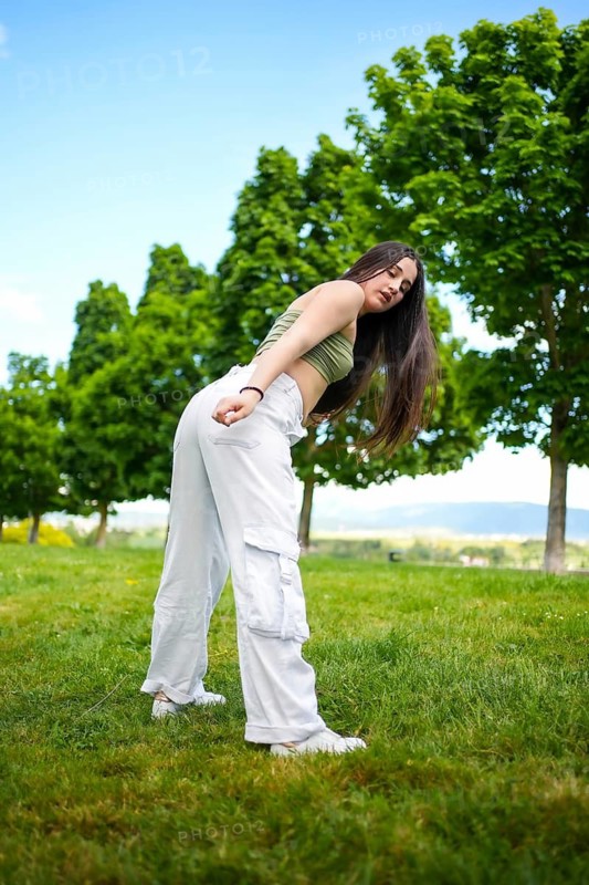 Vertical photo of a caucasian young woman twerking dancing modern music in a park