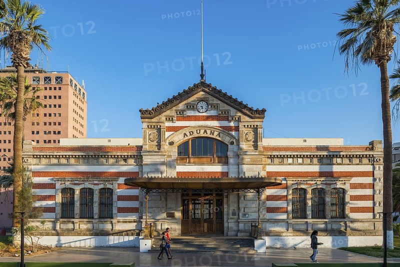 Historic customs building in General Manuel Baquedano Park between palm trees, city of Arica, Chile