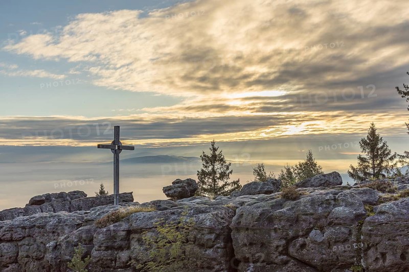 Silhouette of the summit of Mount Töpfer with summit cross, behind it morning sky with clouds and sunbeams, Zittau Mountains, Saxony, Germany