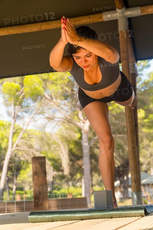 Yoga instructor practicing warrior three pose outdoors, balancing on one leg with hands joined above head, demonstrating balance, strength, and mindfulness in a natural setting