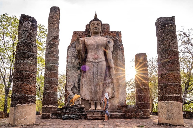Tourist in front of the giant standing Buddha in the temple Wat Saphan Hin, UNESCO World Heritage Sukhothai Historical Park, Thailand