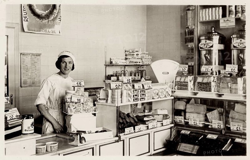 Colonialwaren shop counter, shop, business, profession, twenties, saleswoman, poster, a woman in a shop with cheese specialties and a scale surrounded by shelves, around 1936