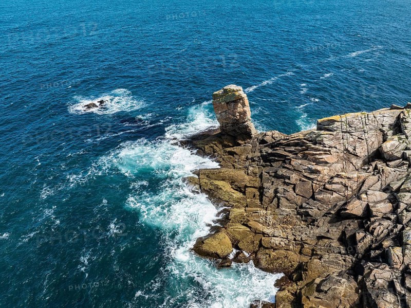 Aerial view of steep granite rocks with a rock tower at Pointe du Raz on the stormy Breton coast, on whose edges the ocean spray breaks white, Plogoff, Cap Sizun, Finistère department, Brittany region, France