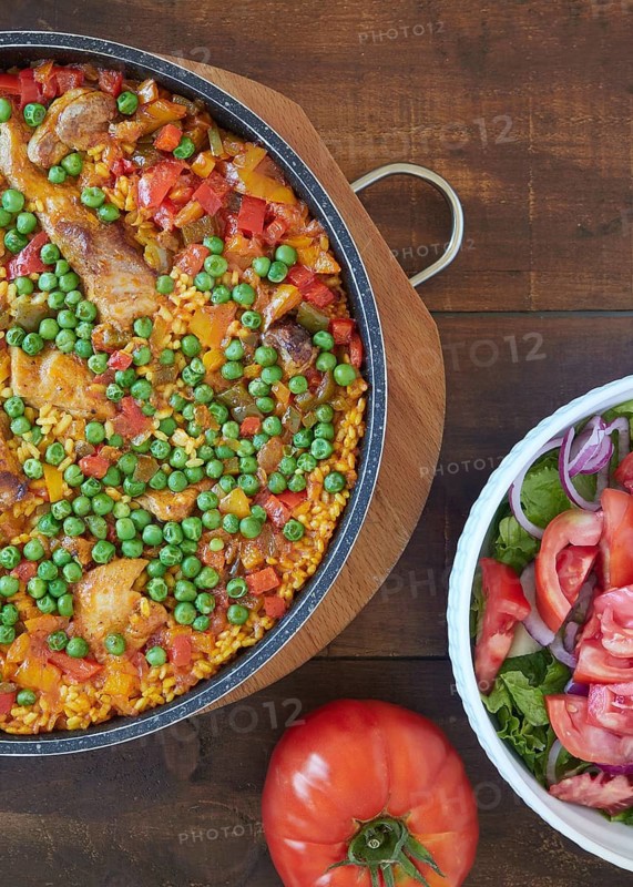 Close up view from above of paella and tomato salad. Rice with pork and chicken, vegetables and peas. Spanish food