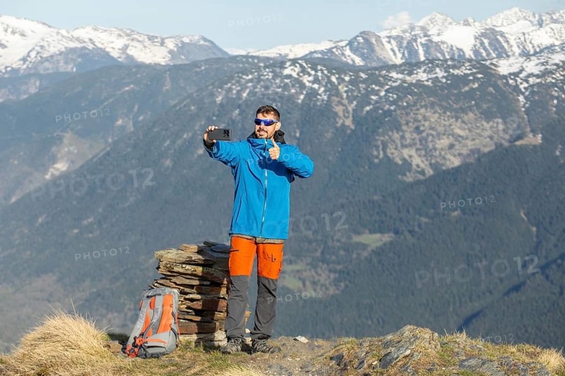 A man enjoys a trek in the Pyrenees, capturing a selfie amidst the stunning mountain backdrop. Dressed in outdoor gear, he stands on a hillside, conveying adventure and freedom