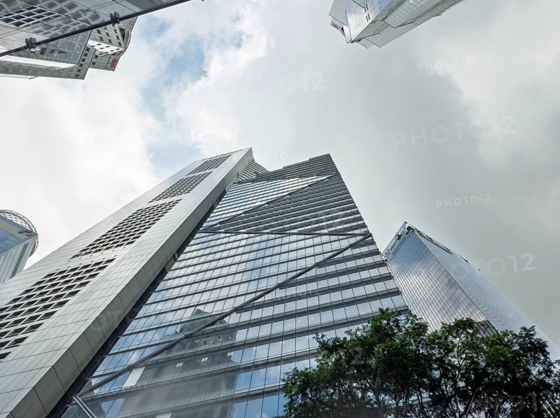 From below a dynamic upward view of towering modern skyscrapers in Singapore, set against a cloudy sky, showcasing urban architecture and design