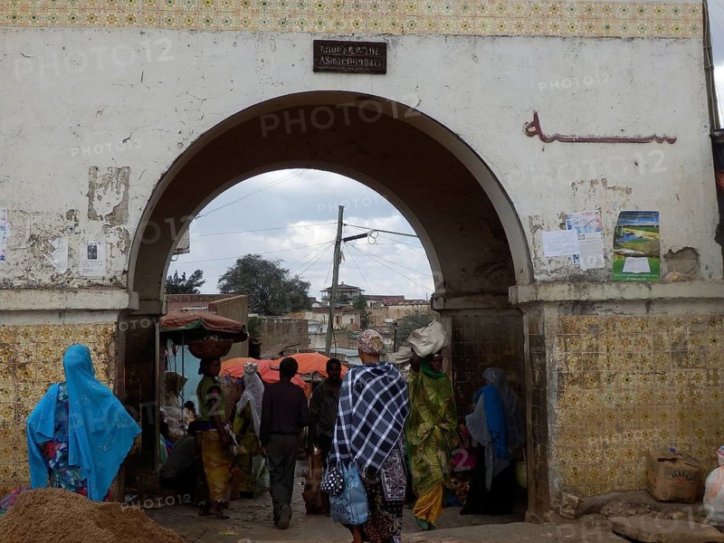 Harar city gate, market scene with people wearing traditional clothes under an archway, Harar, Ethiopia