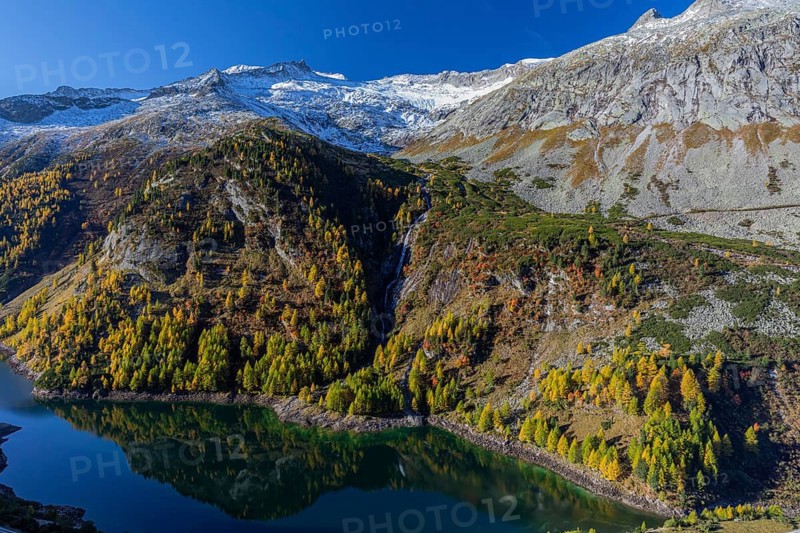 The Galgenbichl reservoir with a mountain forest in fall foliage on a bright sunny morning. Seen from the Malta Hochalm road. Carithia, Austria