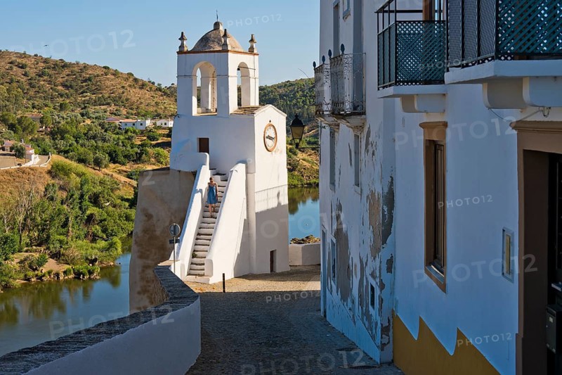 A woman in a blue summer dress climbs the clock tower (Torre do Relogio), which was built in one of the towers of the city walls on the right bank of the River Guadiana. Mertola. Baixo Alentejo. Portugal