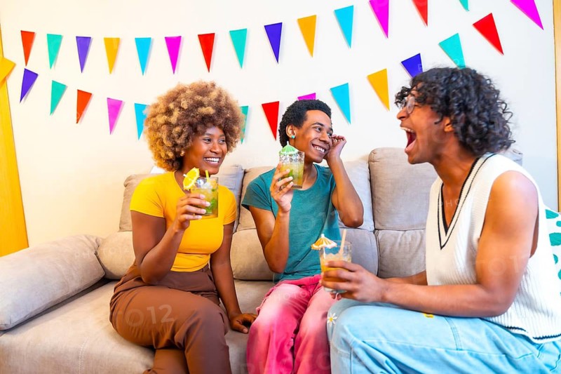Multi-ethnic friends sitting together on the sofa drinking cocktails and having fun at home
