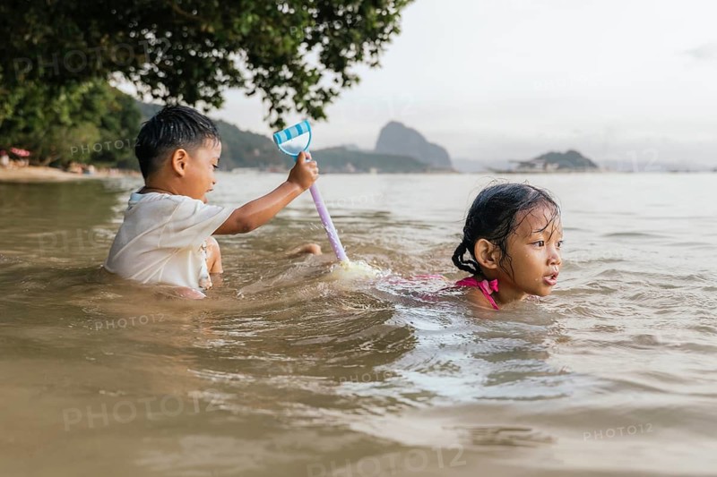 Two children play in the shallow waters of a Philippine beach. A child with short hair holds a toy, while the other, with long hair, swims nearby, showcasing carefree joy