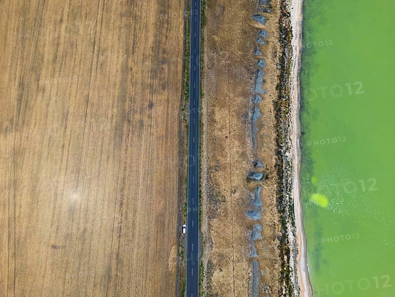 Aerial shot capturing a fascinating contrast, a straight road separates a golden field from a vibrant green lake in Victoria, Australia. The unique colors create a visually stunning landscape
