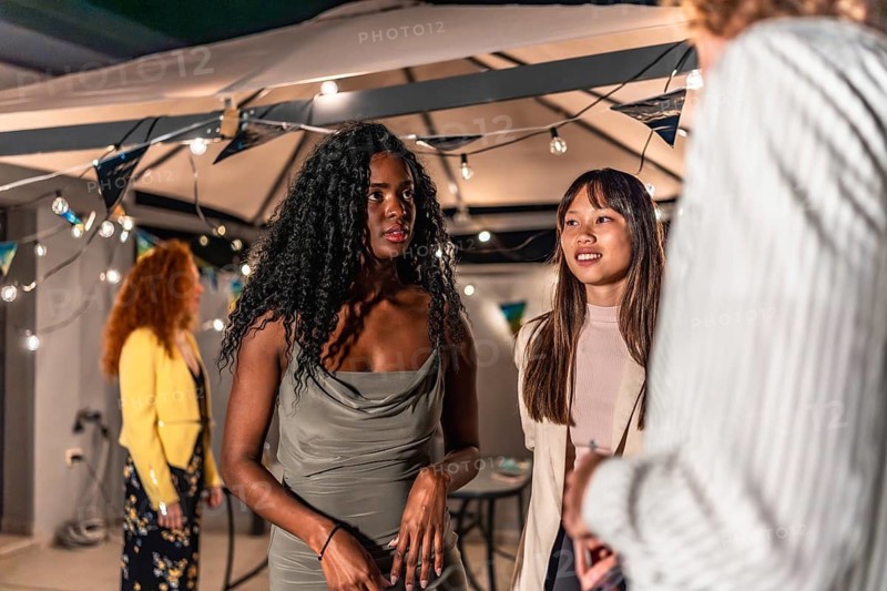 Multi-ethnic fiends dressing elegant clothes chatting calm during night party at terrace