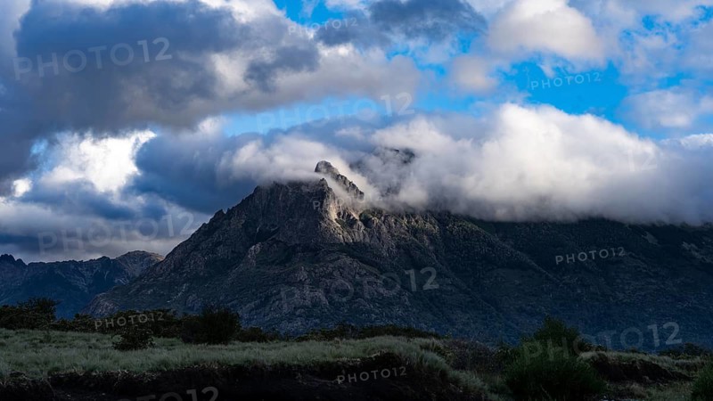 Rocky mountain peak covered in clouds, wooded flanks and grassland in the foreground, Andes, Araucanía region, Chile