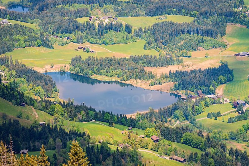 A quiet lake surrounded by forest and small villages in a hilly landscape, Hahnenkamm, Kitzbühel, Austria