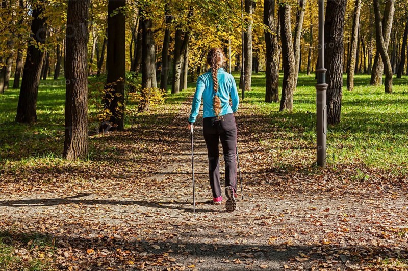 Nordic walking adventure and exercising concept, woman hiking withnordic walking poles in park