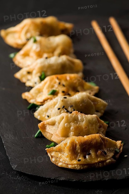 Japanische Gyoza-Knödel, gebraten, mit Soße, auf schwarzem Hintergrund, Draufsicht, ohne Personen, getönt, gekocht, selektiver Fokus