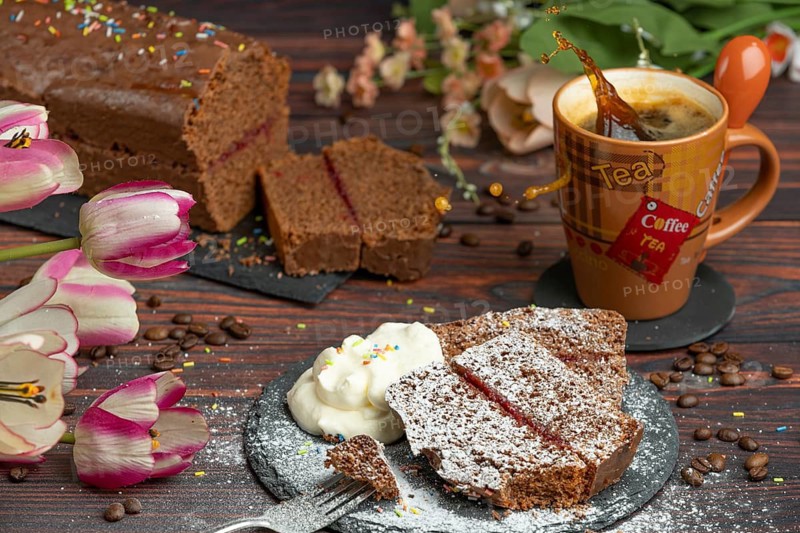 Cake with crumble and icing sugar next to whipped cream and cup with sparkling coffee, flower decoration