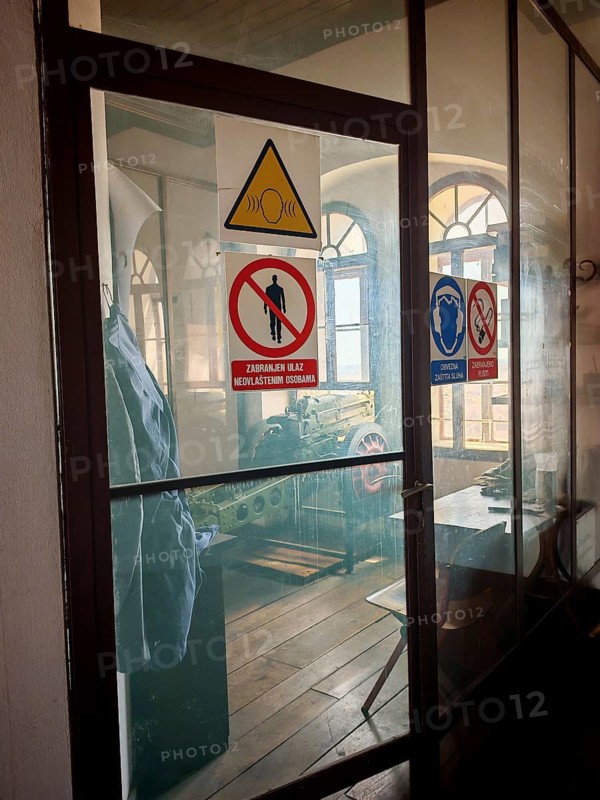 An industrial interior in the Lotrscak Tower with cannon and warning signs behind a glass door, Zagreb, Croatia