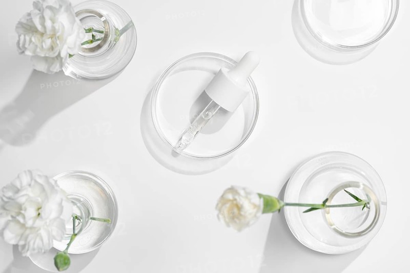 A top view of skincare laboratory equipment with serums and fresh flowers in petri dishes, highlighting the natural components in beauty product development