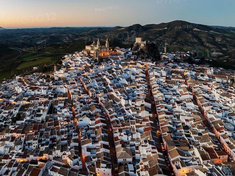 The hilltop White Town of Olvera with its La Encarnación church and Moorish castle. At dusk. Aerial view. Drone shot. Cádiz province, Andalusia, Spain