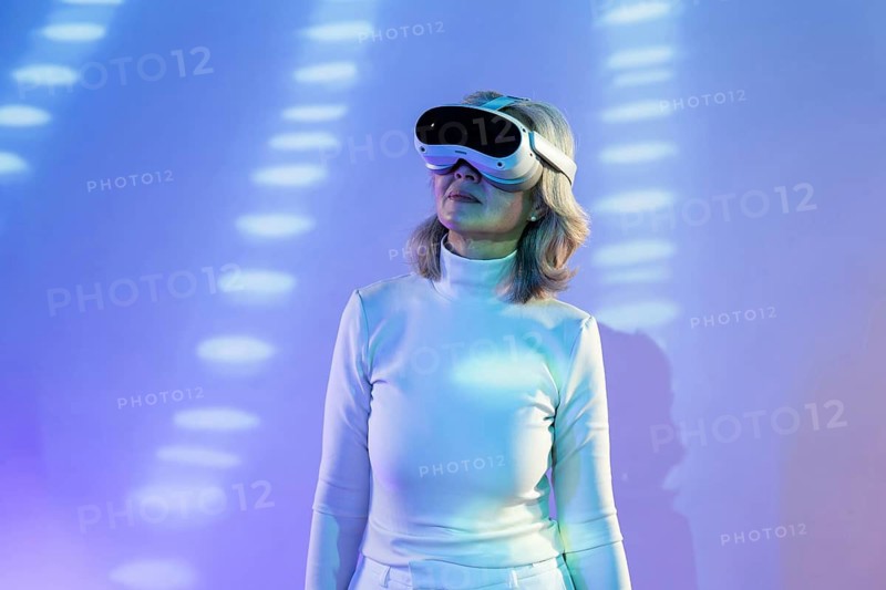 An elderly Asian woman wearing VR goggles, immersed in the metaverse. She explores a digital realm with an intrigued expression, surrounded by colorful light patterns