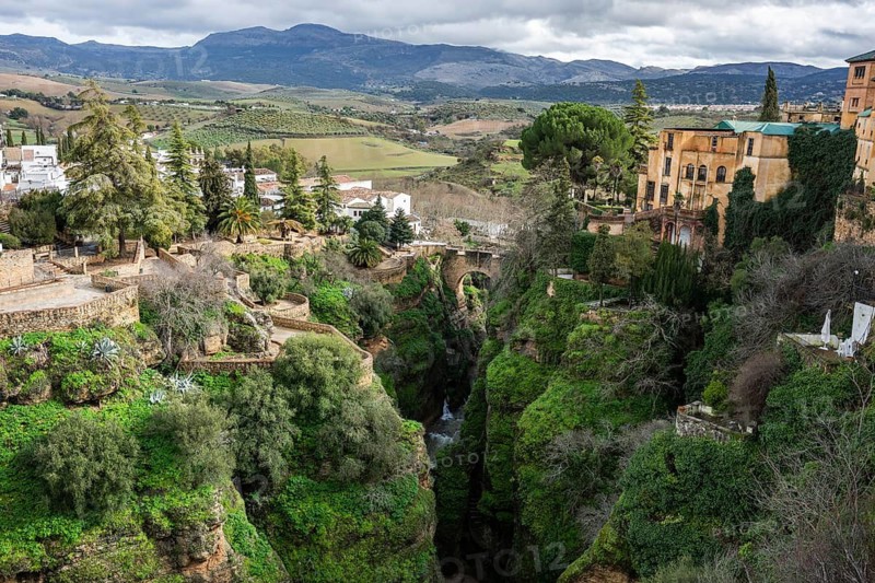High angle panoramic view of the lush El Tajo gorge in Ronda with white houses and historic architecture perched on steep limestone cliffs in Ronda, Spain