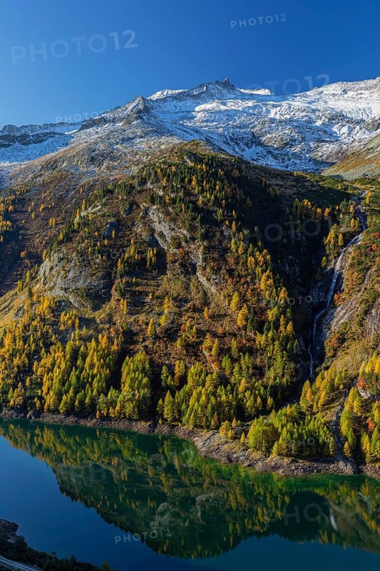 The Galgenbichl reservoir with a mountain forest in fall foliage on a bright sunny morning. Seen from the Malta Hochalm road. Carithia, Austria