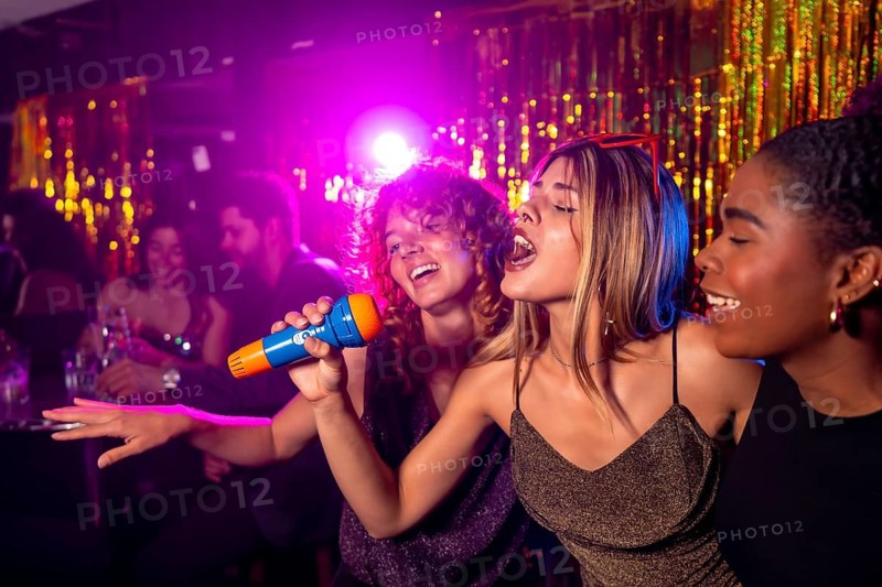 Friends enjoying karaoke night, singing in a nightclub with colorful lights and shiny decorations